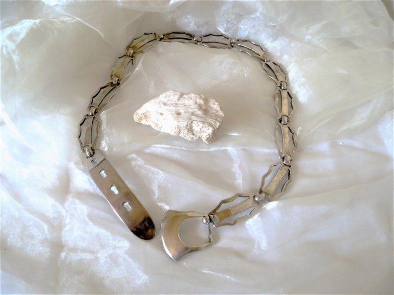 May include: A silver chain belt with a unique geometric design and a large, open buckle.