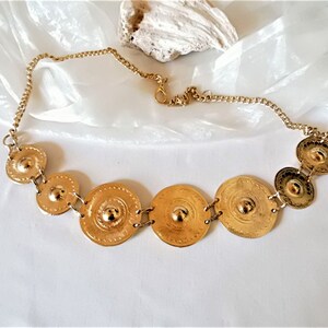 Puede incluir: Un collar de oro con una cadena y varios colgantes redondos de metal en relieve.