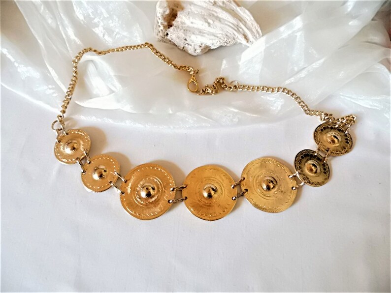Puede incluir: Un collar de oro con una cadena y varios colgantes redondos de metal en relieve.