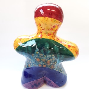 May include: A ceramic figurine with a rainbow design. The figurine is painted in shades of red, yellow, green, blue, and purple. The figurine has a rounded shape and a smooth, glossy finish.