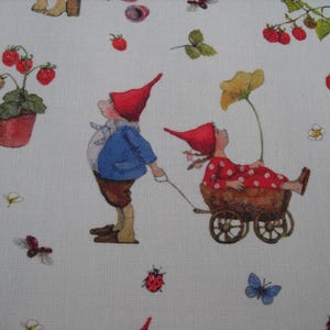 May include: White fabric with a whimsical print featuring gnomes, strawberries, flowers, butterflies, and a snail. One gnome pulls a cart with another gnome inside. The gnomes wear red hats and are surrounded by nature elements.