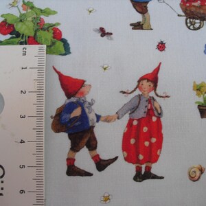 May include: Light blue fabric with a repeating pattern of whimsical gnomes, strawberries, flowers, and insects. The gnomes are depicted in red hats and colorful clothing, holding hands. The fabric is suitable for quilting and crafting projects.