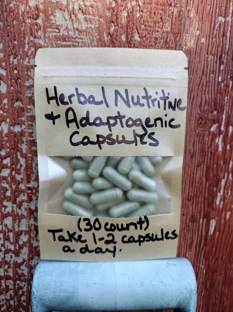 Pu&ograve; includere: Una busta di carta marrone con un'etichetta bianca che recita "Herbal Nutritive + Adaptogenic Capsules (30 count) Take 1-2 capsules a day.". La busta contiene un sacchetto di plastica trasparente pieno di capsule verde chiaro.
