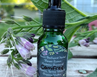 Peut inclure: Une bouteille en verre vert avec un bouchon compte-gouttes noir, étiquetée "Anne's Backyard Herbal Flower Essence Comfrey". L'étiquette comprend des motifs floraux et du texte. La bouteille est de 0,5 oz et est entourée de fleurs et de feuilles de consoude.