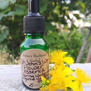 May include: A small green glass bottle with a black dropper top. The bottle is labeled "Anne's Backyard Herbal St. John's Wort Flower Essence Spring Water Organic Extract .5 oz.". Yellow St. John's Wort flowers are in the foreground.