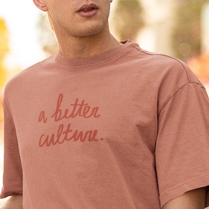 May include: A person wearing a light brown t-shirt with the text "a better culture." printed in red.