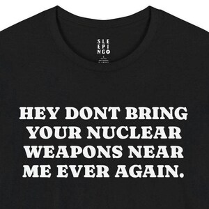 May include: Black t-shirt with white text that reads "Hey don't bring your nuclear weapons near me ever again."