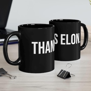 May include: Two black ceramic coffee mugs with white text. The mug on the left says "THANKS ELON." The mug on the right says "THANKS ELON."