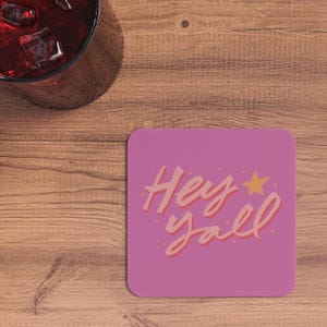 May include: Pink square coaster with the text "Hey y'all" in a pink and orange font with a small yellow star.