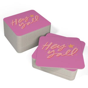 May include: A stack of pink square coasters with the text "Hey yall" in orange lettering and a small yellow star.