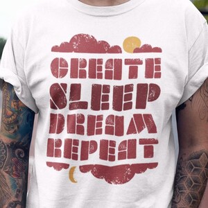 May include: White t-shirt with a red graphic print that says "Create, Sleep, Dream, Repeat". The graphic is in a vintage style with a sun and moon.