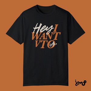 May include: Black t-shirt with the text "Hey I WANT TO" in orange and white lettering.