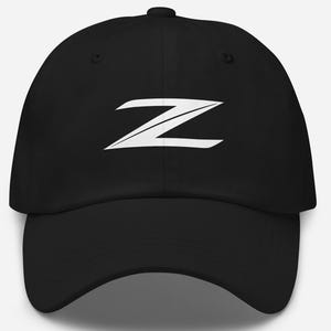 Puede incluir: Gorra de béisbol negra con un logotipo "Z" blanco estilizado en la parte delantera. La gorra tiene una visera curva y una corona estructurada. La correa ajustable asegura un ajuste cómodo. Un accesorio clásico para el uso diario.