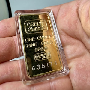 May include: A gold bar with the inscription "CREDIT SUISSE" and "ONE OUNCE FINE GOLD 999.9". The bar also has a stamp with the letters "CH" and the words "ESSAYEUR FONDEUR" and the number "435174".