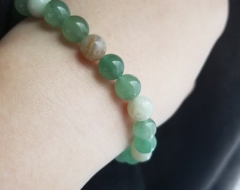 May include: A green and white beaded bracelet with round beads. The bracelet is made of natural stones.