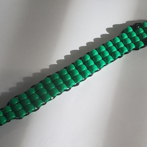 May include: A green beaded bracelet with black string connecting the beads. The bracelet is laid flat on a white surface.