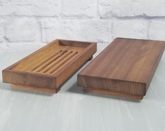 May include: Two wooden trays, one with a slatted design and the other with a smooth surface, are displayed on a light blue table. Both trays are made of dark brown wood.