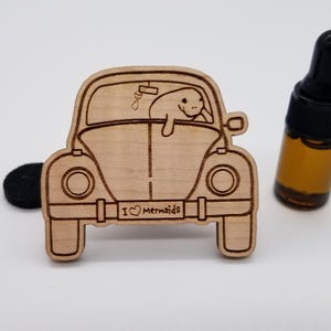 May include: A wooden car air freshener with a manatee peeking out of the window. The car has a license plate that reads "I ♥ Mermaids".