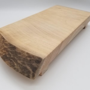 May include: A natural wood serving tray with a live edge and a rectangular shape. The tray is made of light wood with a dark brown bark edge.