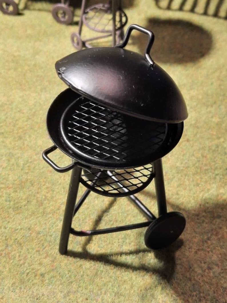 May include: A black metal grill with a lid and a wire rack. The grill is on a tripod stand with wheels.