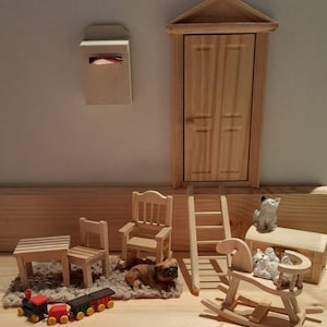 Könnte beinhalten: Ein Holzspielset mit einem Schaukelpferd, einer Leiter, einem Stuhl, einem Tisch, einem Briefkasten, einer Tür und einer Spielzeugeisenbahn. Außerdem gibt es zwei kleine Holzfiguren eines Katers und eines Hundes.