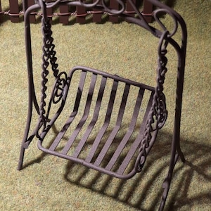 May include: A miniature metal swing set with a black finish. The swing has a decorative, scrolled frame and a slatted seat.