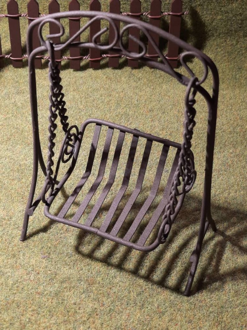 May include: A miniature metal swing set with a black finish. The swing has a decorative, scrolled frame and a slatted seat.