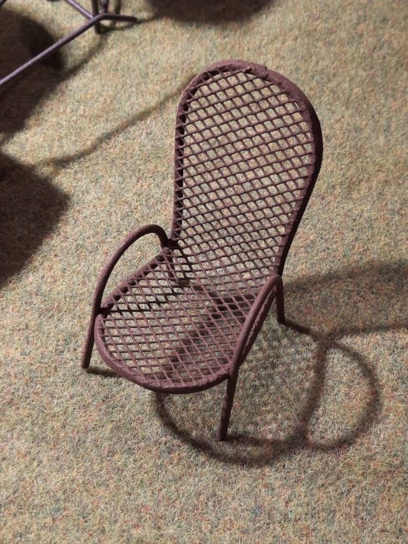 May include: A rusty metal chair with a diamond-shaped wire mesh design. The chair has a curved back and a single armrest.