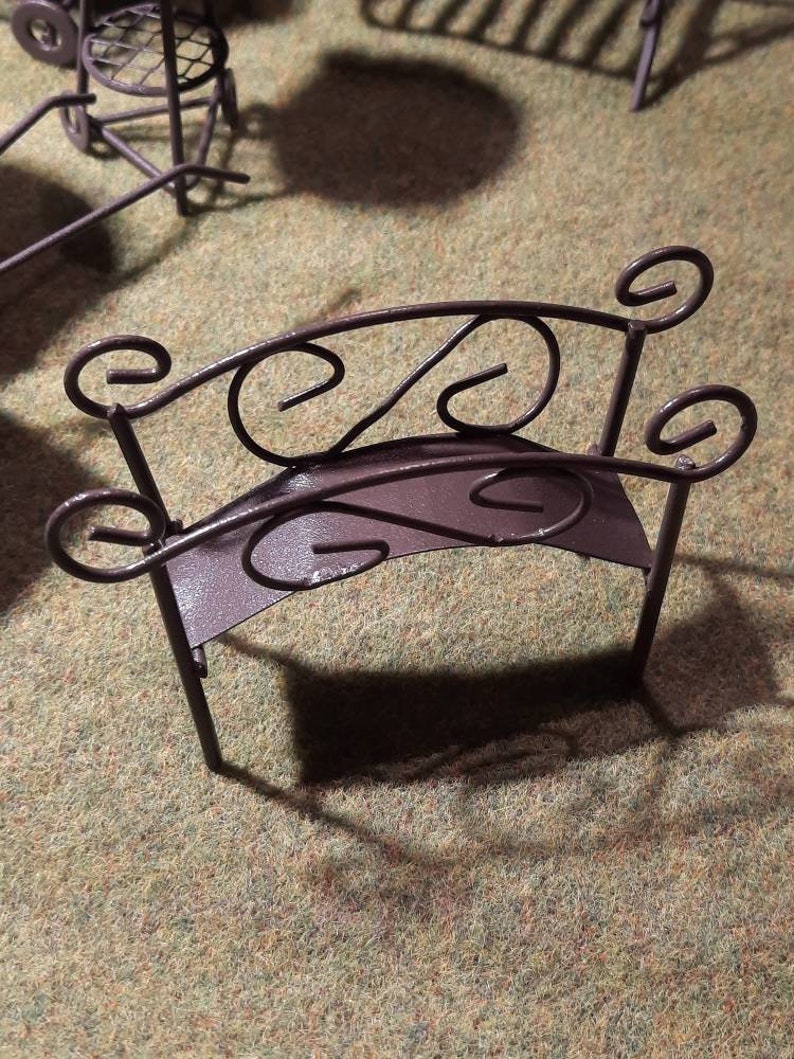 May include: A small, brown metal bench with a decorative, curved back and scrolled details. The bench is made of wrought iron and has a rustic, vintage look.
