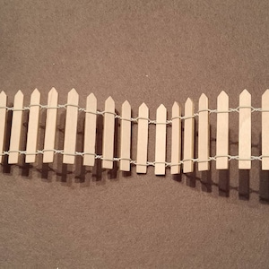 May include: A miniature wooden picket fence with a white string woven through the top and bottom of the fence.