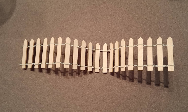 May include: A miniature wooden picket fence with a white string woven through the top and bottom of the fence.