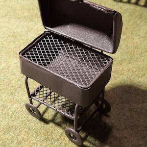 May include: A black metal grill on wheels with a removable lid. The grill has a wire mesh cooking surface and a lower shelf.