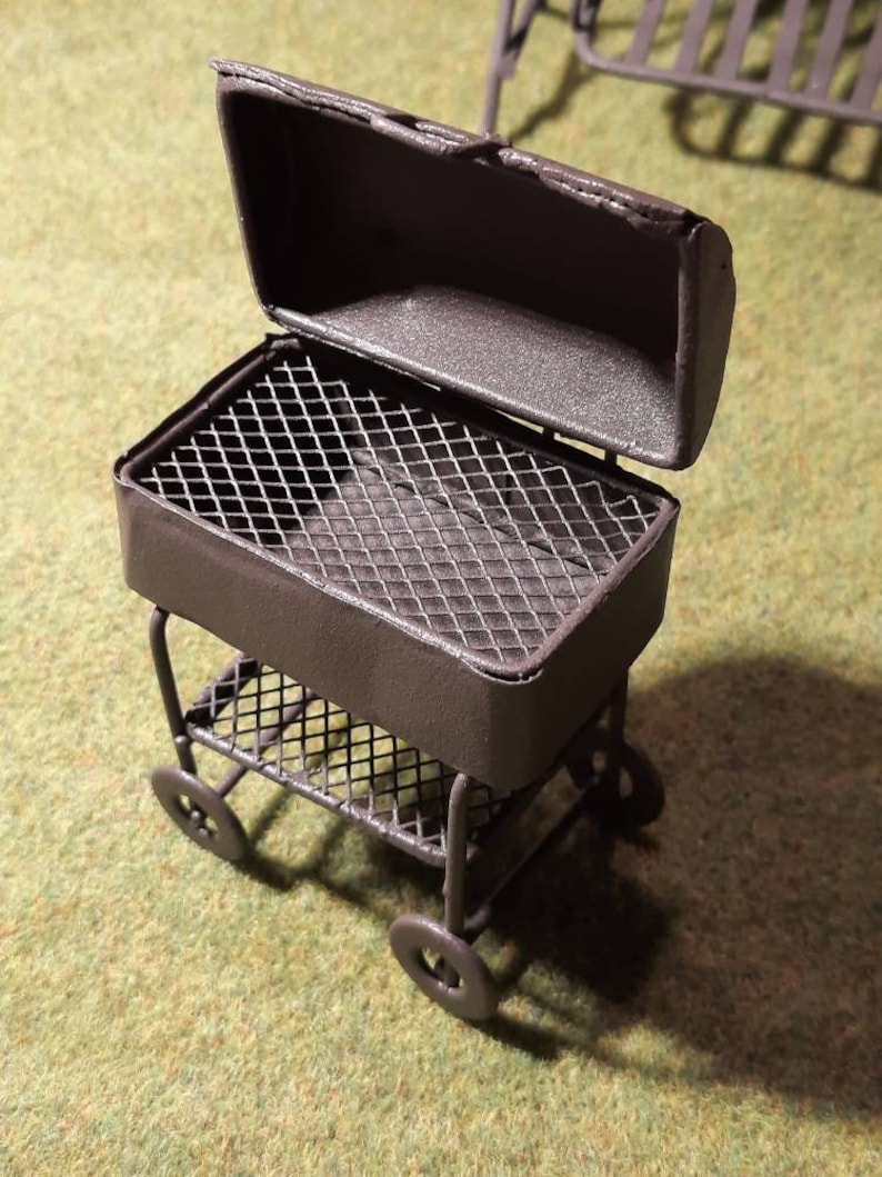 May include: A black metal grill on wheels with a removable lid. The grill has a wire mesh cooking surface and a lower shelf.