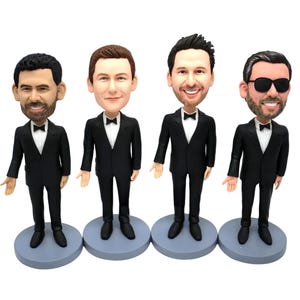 May include: Four custom bobblehead figurines standing on circular grey bases. Each figure depicts a person wearing a black tuxedo with a white shirt and black bow tie. The figures feature distinct facial expressions, hairstyles, and one wears sunglasses.