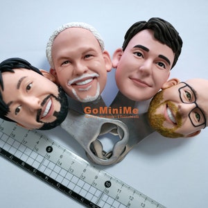 May include: Four custom-made cake toppers, each a realistic portrait of a person's head, are attached to a silver bottle opener. The bottle opener has the text "GoMiniMe" and "Mini cake toppers & Babbleheads".