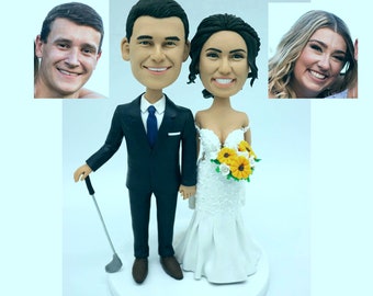Op de afbeelding: Een bruidstaarttopper met een bruid en bruidegom in een fantasierijke, cartoonachtige stijl. De bruidegom houdt een golfclub vast en de bruid houdt een boeket zonnebloemen en witte bloemen vast.