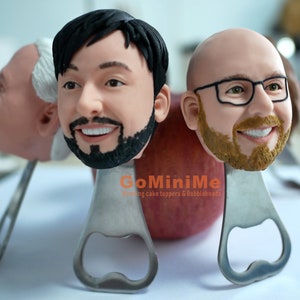 May include: Three personalized bottle opener cake toppers with the text "GoMiniMe Wedding cake toppers & Bobbleheads". The toppers are made of a brown, beige, and black material and are shaped like human heads.