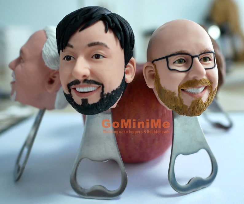 May include: Three personalized bottle opener cake toppers with the text "GoMiniMe Wedding cake toppers & Bobbleheads". The toppers are made of a brown, beige, and black material and are shaped like human heads.