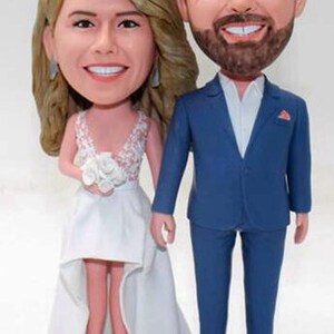 May include: A wedding cake topper featuring a bride and groom in a caricature style. The bride is wearing a white dress with a lace bodice and a bouquet of white flowers. The groom is wearing a blue suit with a white shirt and a red pocket square.