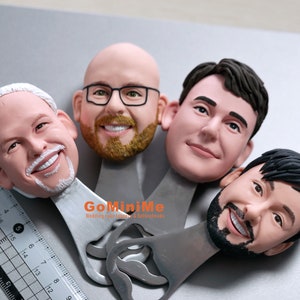 May include: Four personalized bottle openers with a silver finish. Each opener features a 3D sculpted face with realistic details. The text "GoMiniMe Wedding cake toppers & Bobbleheads" is printed on the opener.