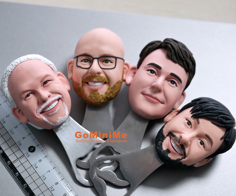 May include: Four personalized bottle openers with a silver finish. Each opener features a 3D sculpted face with realistic details. The text "GoMiniMe Wedding cake toppers & Bobbleheads" is printed on the opener.