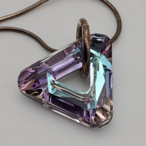 May include: A silver chain necklace with a triangular pendant made of iridescent crystal. The crystal is a mix of purple, blue, and green.