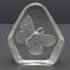 Könnte beinhalten: Ein durchsichtiger Glas-Briefbeschwerer mit einem erhabenen Schmetterlingsmotiv. Der Schmetterling ist mit Adern detailliert und hat eine strukturierte Oberfläche.