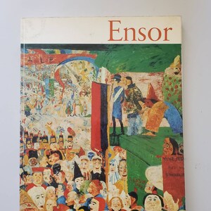 May include: A book cover with the title "Ensor" in red letters. The cover features a colorful painting of a crowd of people wearing masks and costumes. The painting is set in a street scene with buildings and a sky in the background.
