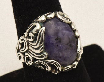 Könnte beinhalten: Ein silberner Ring mit einem verzierten Design, das einen großen, ovalen, violetten Edelstein zeigt.