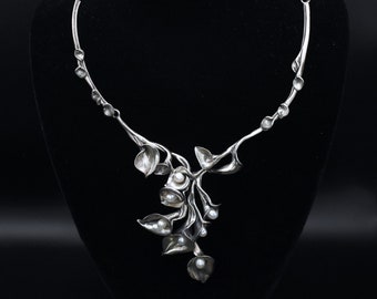 May include: A silver necklace with a delicate floral design featuring small white pearls. The necklace is made of a twisted silver chain with a pendant that resembles a cluster of flowers.