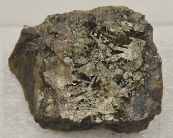 Può includere: Primo piano di una roccia ruvida di colore grigio scuro con un gruppo di cristalli lucenti, metallici, di colore grigio argento.