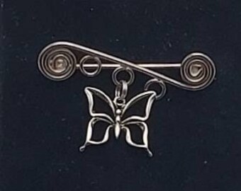 May include: A silver butterfly charm hangs from a silver wire brooch. The brooch is made of twisted wire and has a spiral design at each end.