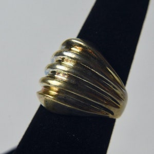 May include: A gold and silver ring with a ridged design. The ring is on a black display stand.