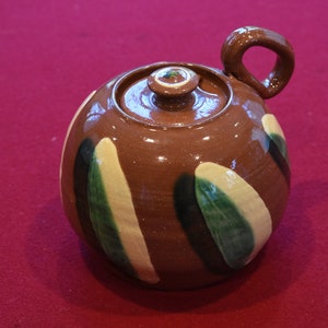 Op de afbeelding: Een bruine theepot van keramiek met een rond lichaam en een handvat. De theepot is versierd met groene en gele geverfde strepen.